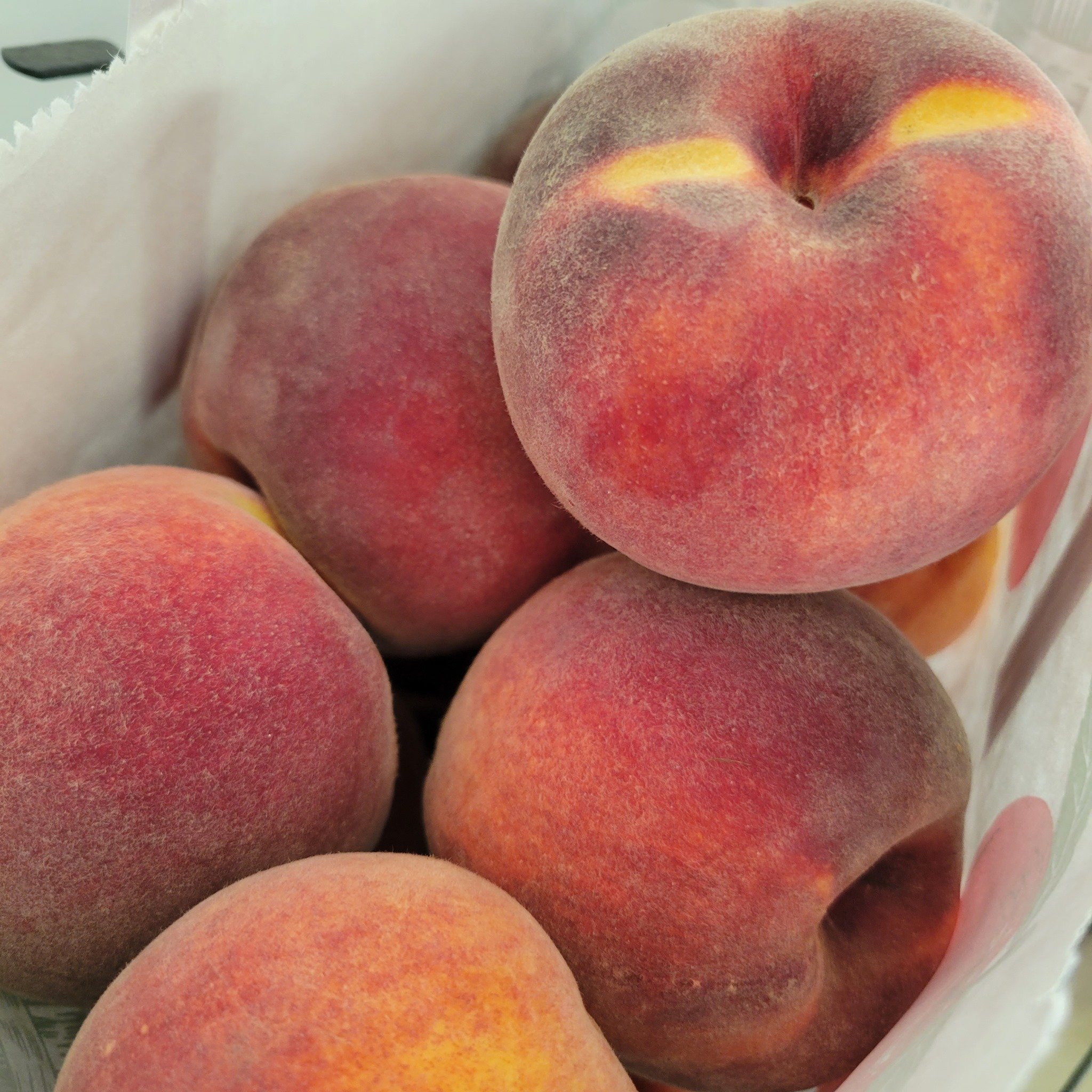 Fresh, ripe peaches with a fuzzy skin and vibrant red and yellow hues, arranged in a basket, showcasing their juicy texture and seasonal appeal. Perfect for summer recipes and healthy snacking.